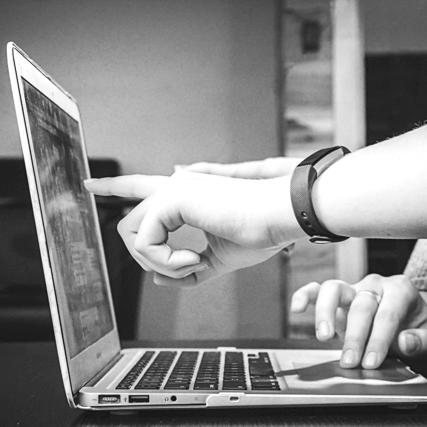 Zusammenarbeit event-akademie.at I Foto in schwarz/weiß, das einen Laptop zeigt, an dem zwei Personen arbeiten und auf etwas am Bildschirm deuten.
